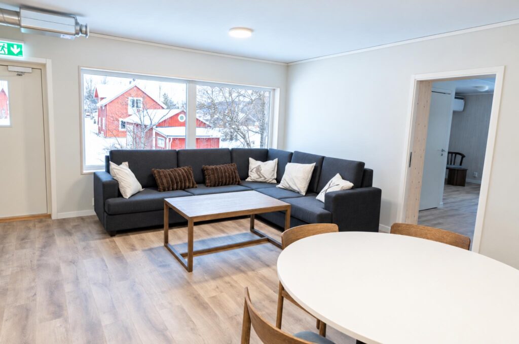 Gemensamt tv-rum med stor soffa och fönster mot röda hus i snön